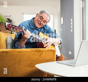 Homme senior portant des lunettes jouant de la guitare sur un canapé dans la salle de séjour Banque D'Images