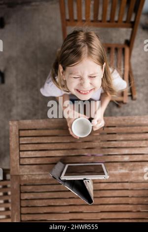 Fille souriante avec tasse à lait et tablette PC sur table Banque D'Images