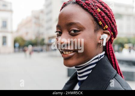 Femme souriante écoutant de la musique avec un casque intra-auriculaire sans fil Banque D'Images