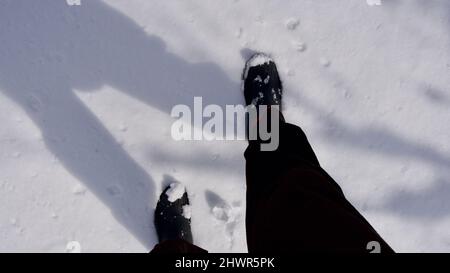 Homme marchant sur un terrain enneigé. Homme marchant avec des bottes sur ses pieds. Banque D'Images