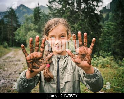 Fille souriante montrant des mains boueuses dans la forêt