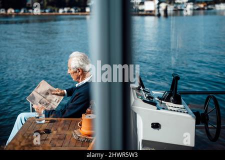 Homme senior lisant le journal à la péniche le jour ensoleillé Banque D'Images