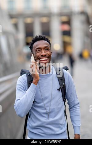 Un jeune homme heureux portant un sac à dos parlant sur un téléphone portable Banque D'Images