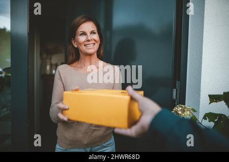 Une femme heureuse reçoit le colis de la personne de livraison à la porte Banque D'Images