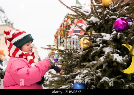 Fille portant un chapeau tricoté rayé touchant l'arbre de Noël Banque D'Images