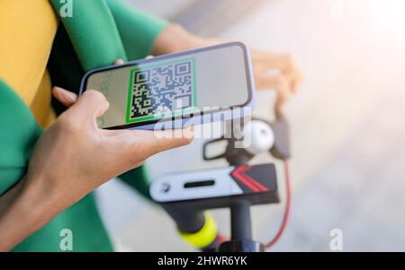 Commuter scannant le code QR via un smartphone sur un scooter électrique Banque D'Images