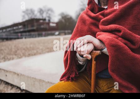 Homme senior tenant une canne à pied enveloppée dans une couverture assis à la plage Banque D'Images