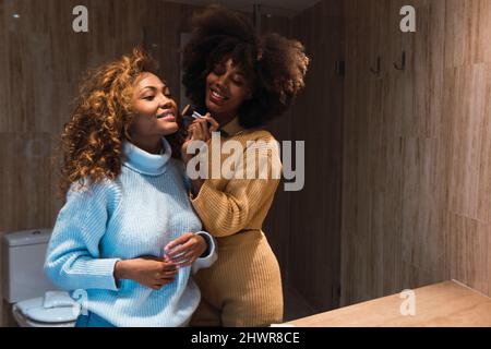 Femme appliquant un fard à joues à un ami dans la salle de bains à la maison Banque D'Images