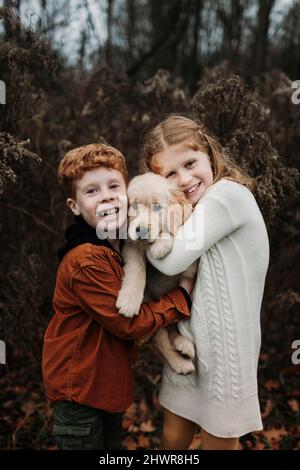 Heureux frères et sœurs qui embrassent le chiot Golden Retriever en forêt Banque D'Images