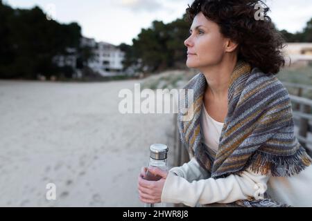 Femme avec bouteille d'eau à la plage en hiver Banque D'Images