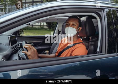 Homme dans un masque facial protecteur conduisant une voiture dans l'épidémie de COVID-19 Banque D'Images