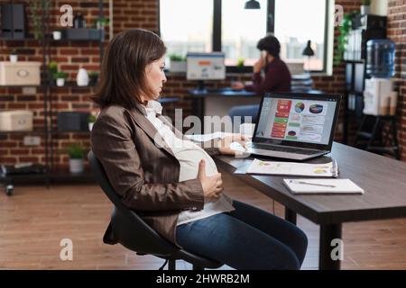 Future mère travaillant sur le diagramme financier de l'entreprise, le développement de nouvelles stratégies de marketing et l'analyse de rapport statistique. Femme enceinte surveillant la croissance économique et la présentation du projet. Banque D'Images