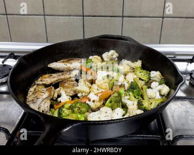 Brocoli, carottes, chou-fleur et poulet mélangés à des herbes, poivre et sel cuits sur une poêle en fonte. Banque D'Images