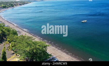 Lagon calme avec bateau à voile et bâtiments en forêt sur le flanc d'une colline. Bateaux traditionnels en bois sur une plage déserte près d'Amed dans le nord de Bali Banque D'Images