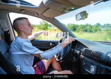 Un jeune homme caucasien avec un bras amputé et une prothèse conduit une voiture Banque D'Images