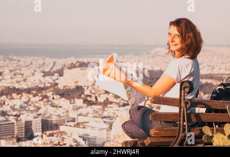 Femme avec une carte assise sur la colline de Lycabette, le point le plus haut de la ville surplombant Athènes avec l'Acropole - voyageur du monde Banque D'Images