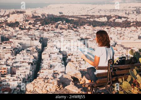 Femme avec une carte assise sur la colline de Lycabette, le point le plus haut de la ville surplombant Athènes avec l'Acropole - voyageur du monde Banque D'Images