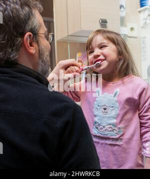 papa aide sa petite fille à se brosser les dents en la faisant tenir correctement la brosse à dents Banque D'Images