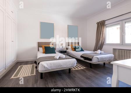 Chambre avec lits doubles, parquet en bois sombre, coussins, têtes de lit rembourrées et armoire intégrée avec portes blanches Banque D'Images