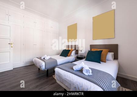 Chambre avec lits simples, parquet foncé, coussins, têtes de lit rembourrées et armoire intégrée avec portes blanches, couvre-lits assortis et roul Banque D'Images