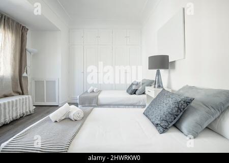 Chambre avec lits simples, parquet foncé, coussins bleus et gris, couvre-lits blancs, couvertures rayées et armoire avec cinq portes en bois Banque D'Images