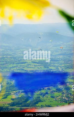 Parapentes survolant la vallée (montagnes des Alpes à l'arrière-plan) vues à travers les drapeaux colorés non focalisés agitant dans le vent. Région du lac d'Annecy (haute-sa Banque D'Images