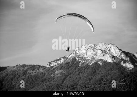 Parapentes volant en tandem et montagnes de Savoie en arrière-plan. Lac d'Annecy, France. Photo historique noir blanc. Banque D'Images