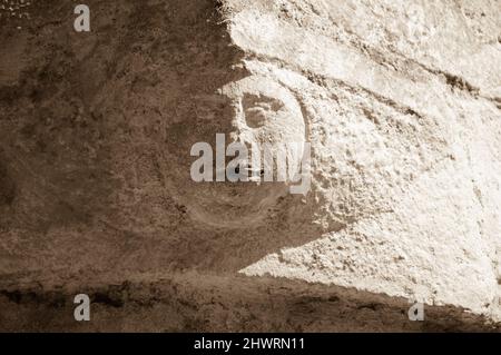 Dépendance au tabagisme. Face humaine en pierre (détail architectural de l'ancien bâtiment) avec une vraie cigarette dans la bouche. Photo conceptuelle historique sépia. Banque D'Images