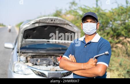 Portriat tir mécanicien de voiture se baladant devant borken avec masque médical sur le bord de la route en regardant la caméra - concept de service de voiture mobile et Banque D'Images