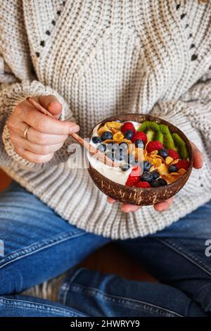 Petit déjeuner sain à la maison. Femme assise sur le sol et mangeant du yaourt avec des fruits et des flocons de maïs. Plats végétariens Banque D'Images