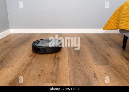 Un aspirateur robot moderne nettoie les panneaux en vinyle de la chambre, un robot de nettoyage autonome. Banque D'Images