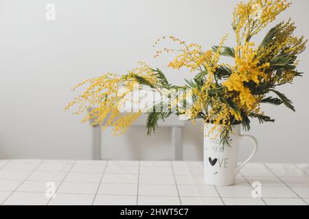 Bouquet de fleurs mimosa jaunes dans un vase sur fond blanc. Banque D'Images