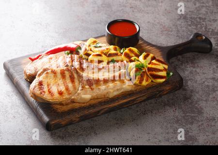 Côtelettes de porc au barbecue maison et pommes de terre grillées prêtes à manger sur un panneau de bois sur la table de clôture. Horizontale Banque D'Images