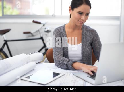 Elle est respectueuse de l'environnement et talentueuse. Photo d'une jeune femme designer travaillant sur son ordinateur portable avec une bicyclette en arrière-plan. Banque D'Images