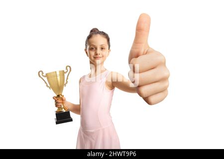 Jolie ballerine petite fille dans une robe rose tenant une tasse de trophée d'or et en faisant des gestes de pouces isolés sur fond blanc Banque D'Images