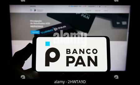 Personne tenant un téléphone mobile avec le logo de la banque commerciale brésilienne Banco Pan sa à l'écran en face de la page Web d'affaires. Mise au point sur l'affichage du téléphone. Banque D'Images