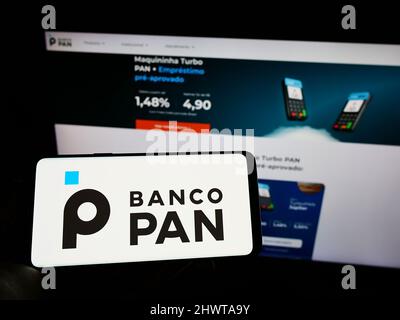 Personne tenant le téléphone portable avec le logo de la banque commerciale brésilienne Banco Pan S.A. à l'écran en face de la page Web des affaires. Mise au point sur l'affichage du téléphone. Banque D'Images