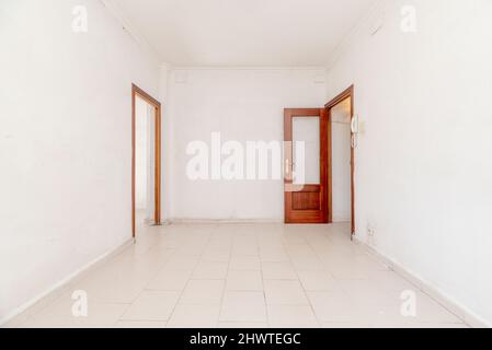 Salle de séjour vide avec deux portes en acajou aux murs blancs et sol en grès blanc Banque D'Images