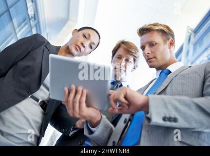 Comme vous le pouvez, nous devrons améliorer nos ventes au cours du prochain trimestre Vue en contre-plongée d'un jeune homme d'affaires montrant quelque chose à ses collègues sur une tablette. Banque D'Images