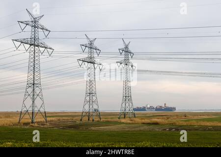 01 mars 2022, Schleswig-Holstein, Brunsbüttel : stand de pylônes électriques sur l'Elbe à Brunsbüttel, sur lequel navigue un bateau à conteneurs. Photo: Frank Molter/dpa Banque D'Images