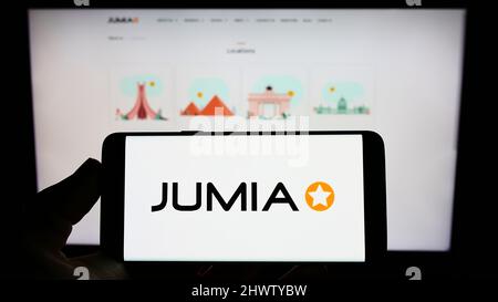 Personne tenant un téléphone portable avec le logo de la société nigériane Jumia technologies à l'écran en face de la page Web d'affaires. Mise au point sur l'affichage du téléphone. Banque D'Images