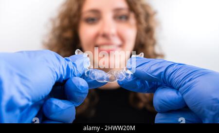 Orthodontiste médecin en gants tenant des étrésillons transparents invisibles en silicone montrer à la femme en clinique dentaire. Bonne fille avec des dents correctrices. Traiteurs Banque D'Images