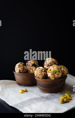 Boules d'énergie faites de fruits secs, pistaches, avoine, et graines comme en-cas dans un bol en bois sur fond noir Banque D'Images