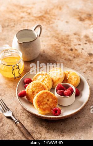 Crêpes au fromage cottage, syrniki au miel et framboise fraîche sur fond texturé Banque D'Images