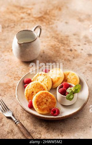 Crêpes au fromage cottage, syrniki au miel et framboise fraîche sur plaque de céramique sur fond texturé Banque D'Images