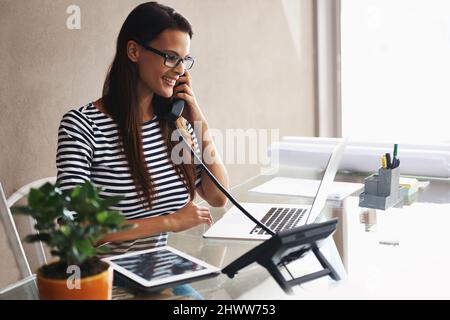 Shes le réceptionniste... et tout le reste. Photo d'une jeune femme d'affaires parlant au téléphone tout en travaillant sur son ordinateur portable. Banque D'Images