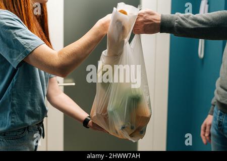 Gros plan d'une jeune femme méconnue qui reçoit un sac d'épicerie contenant des aliments sains de la part du liveur à deux pas de l'appartement. Banque D'Images