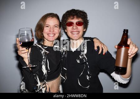 Portrait de jeune couple insouciant qui fait la fête et regarde l'appareil photo tenant des boissons, tourné avec flash Banque D'Images