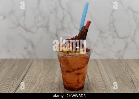 Délicieux smoothie mangoneada glacé au goût de mangue froide avec des morceaux de fruits servis dans une tasse à emporter avec une cuillère et de la paille. Banque D'Images