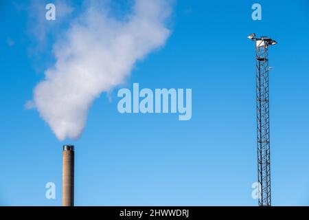 Helsinki / Finlande - 26 FÉVRIER 2022 : grand mât de lumière et un fume avec gaz d'échappement contre un ciel bleu vif Banque D'Images